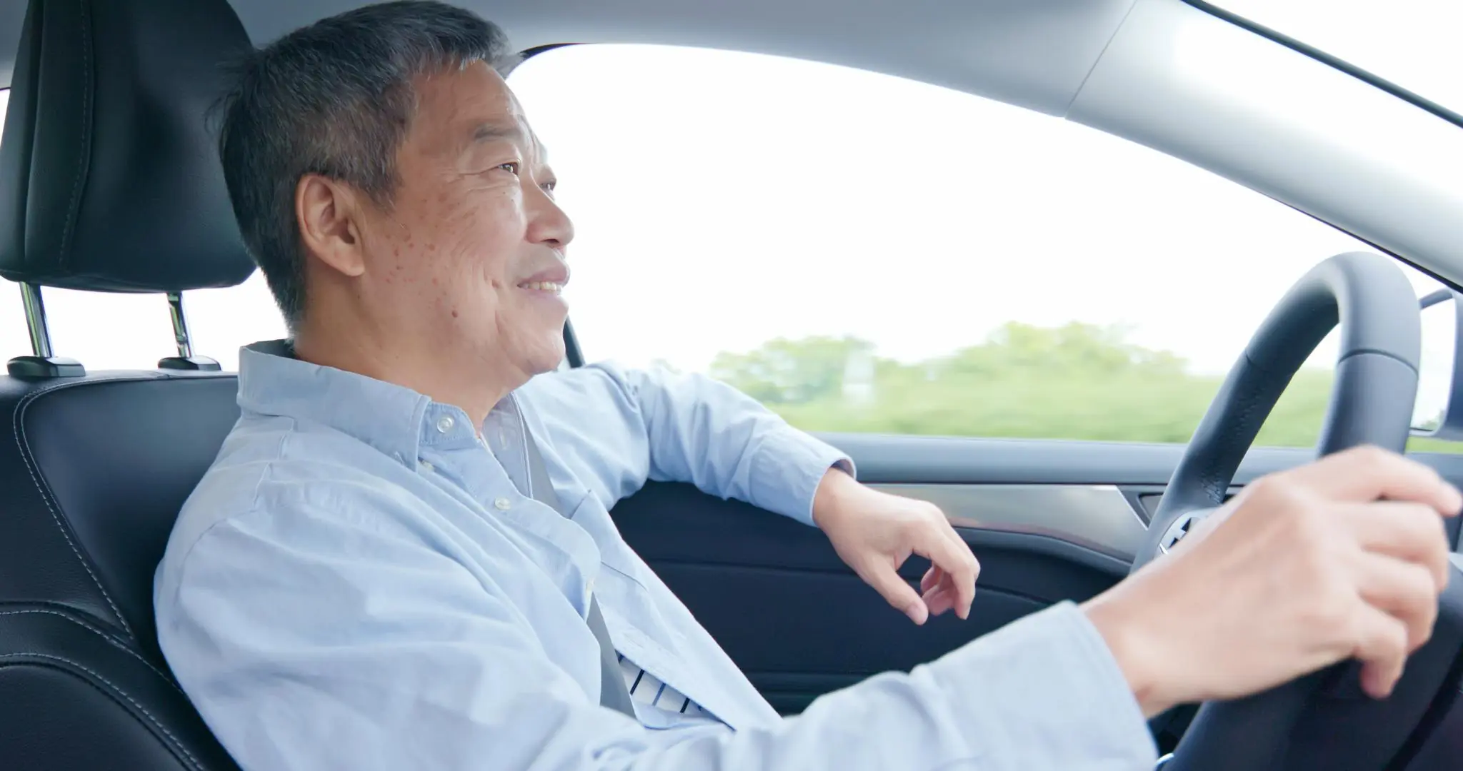An elderly Asian man driving safely on the road, showing the importance of regular eye exams.